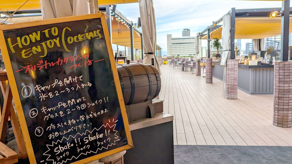 a sidewalk chalkboard sign for a restaurant in Japan. The title is in English: how to Enjoy Cocktails, but everything else on the chalkboard is written in Japanese, except for at the bottom it says Shake! Shake!