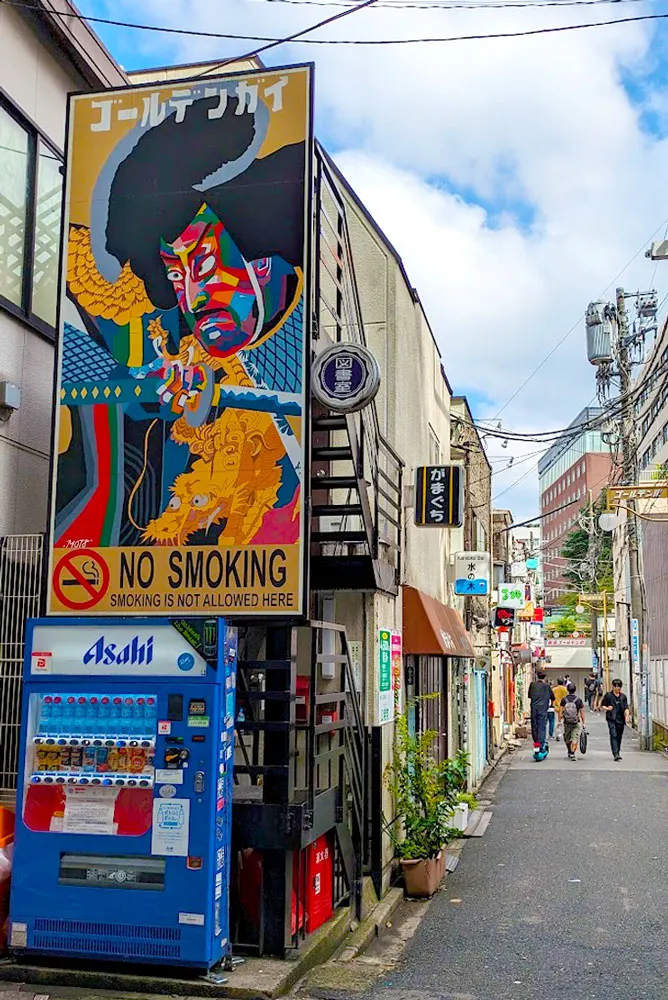 the streets in Tokyo Japan, there's a beautiful mural with some Japanese writing on top. Underneath it it reads, in English, No smoking. And there's a vending machine for Asahi beer below