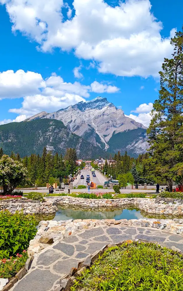 a stone path way surrounds a manmade pond above the streets and a bride leading towards town. In the distance, passed the town, is a giant mountain , taking over the sky. making you realize how small you are. 