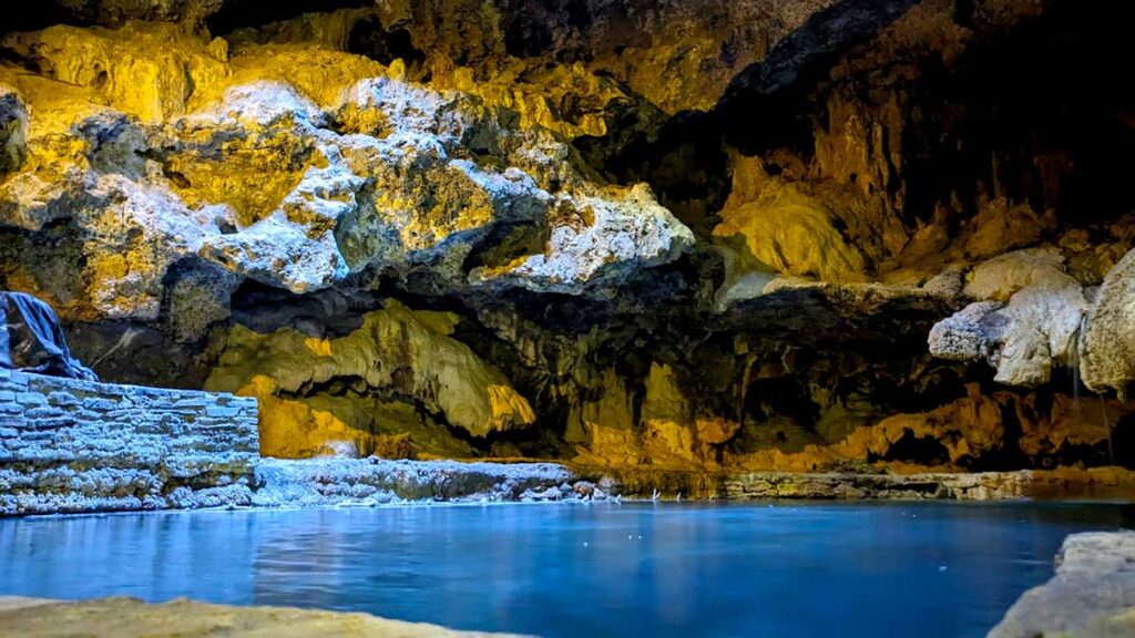 the original natural hot spring in a cave in banff national park. The water is still a vibrant blue colour even though it's in a dark cave. The rock walls are creepy looking, very dark with a yellow hue from the light shining 