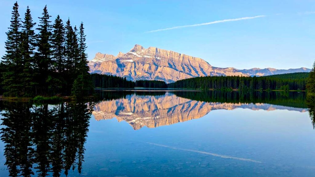 a perfect reflection in a lake of a section of trees on the left, leading into a rocky mountain and then more trees below. 