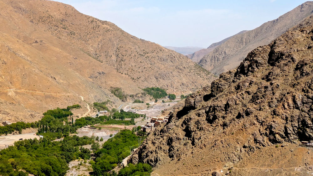 A valley of rocky mountains, where some green lush trees can still survive in the middle - otherwise it would have truly looked like desert mountains. There are roads through the trees below but not much else. When you look closely at the closest rock mountain, you can make out some buildings on the edge of the same colour. 