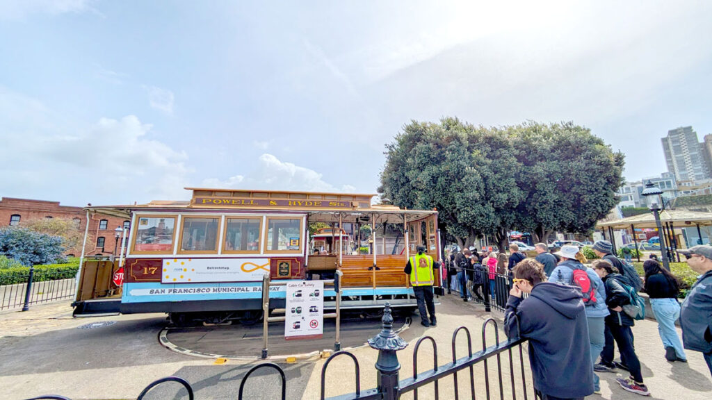 the powell hyde cable car turnaround. there's an iron black fence separating the cable car and the crowds that have already started to form a line around it.