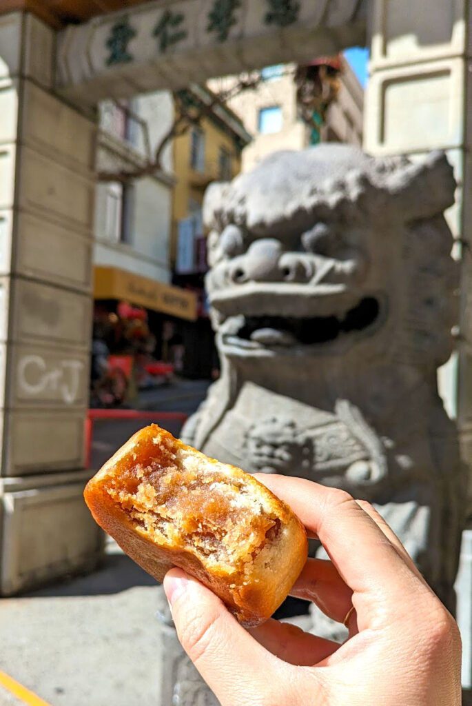 eating your way through San Franciscos chinatown with a moon cake in hand. A bite was taken out of it to show the inside, which his a filled hard cream with a pastry like outside. You know you're in chinatown because theres a Chinese stone dragon behind the moon cake