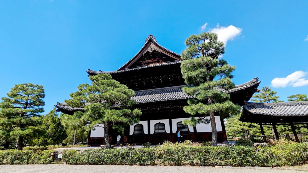 kenninji temple in kyoto, is a classic style buddhist temple with dark brown rooms and trimmings and white on the bottom. Trees grew in front of the temple, but there are also small tea bushes lining the sides.