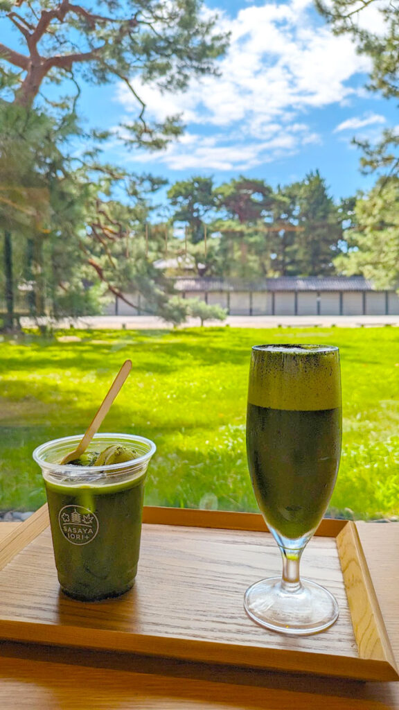 just two examples of matcha flavoured drinks to try in Japan - an iced matcha with matcha ice cream inside, and a matcha beer which looks like a frothy matcha. They sit on a wooden tray overlooking the green grass outside, trees, and blue skies