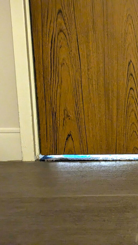 a vertical photo showing a 3 inch between the door and the floor, it allows light and noise into the hotel room.