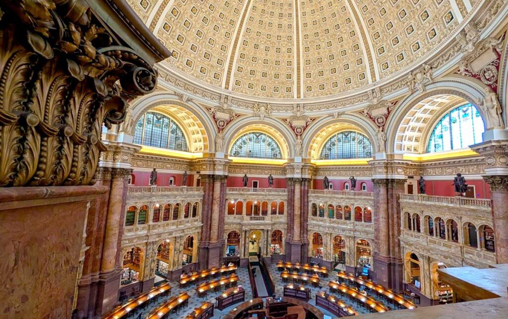 the gorgeous Library of Congress rotunda, with a domes patterned ceiling, there are stained glass windows and statues lining every wall with archways and only at the bottom are there desks for studying. The colours are a rich brown and burgundy red. 
