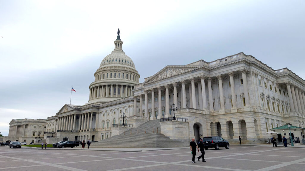 the capitol of the united states building, it looks like a regular capitol building, all in white, with a large rotunda in the middle. Two people walk off, otherwise, there is no one else in view.