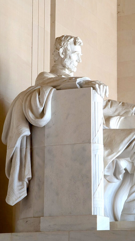 a closeup of the statue of abe lincoln in washington dc and he is looking out on the national mall. It's made of marble stone, very white. This is the side view, where he looks really serious. His hand is place on the side of the chairs