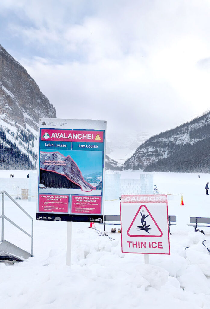 a giant sign stands huge in front of lake louise and the glacial mountains behind it. It says it red: Avalanche , with a diagram of where the risk is on the mountain. 