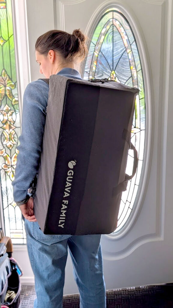 a woman stands with her back to the camera, she's about to walk out the front door. The Guava Family backpack sits on her back, it's pretty much the size of her back, going from the bottom of her neck until just above her bum. 