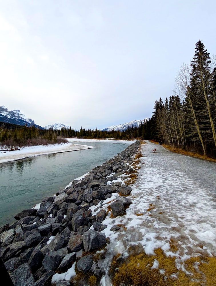 The blue glacial bow river leads your eye from the bottom left corner to the middle. Along the river runs a rock wall, and then a walking path - that is now completely covered in ice. These lines lead your eye to the middle which is separate by ever green trees, then mountains, before reaching the sky. 