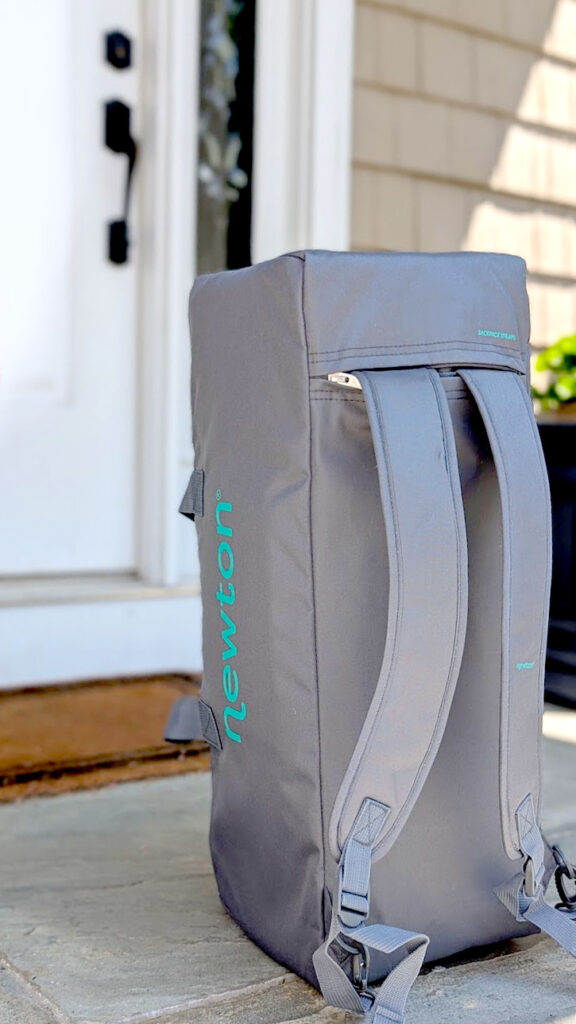the newton travel crib backpack, you can see the strands are coming out of the bag. It sits in the front of a door, outside of a house, just waiting to be picked up.