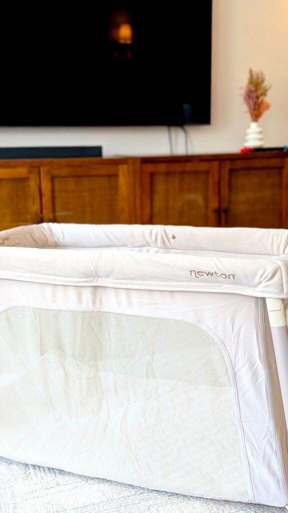 a closeup of the newton travel crib where you can now clearly see the name, newton on the top of the travel crib, written in a darker, complimentary beige brown. 