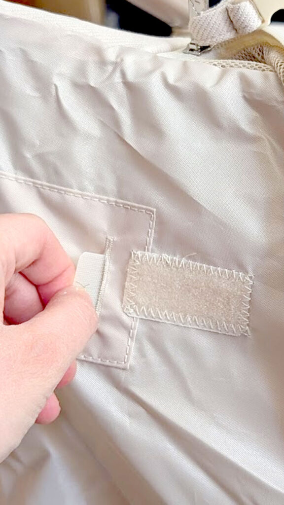 closeup of the velcro underneath the newton travel crib, with a hand that is holding the tab from the mattress that needs to be attached to it. 